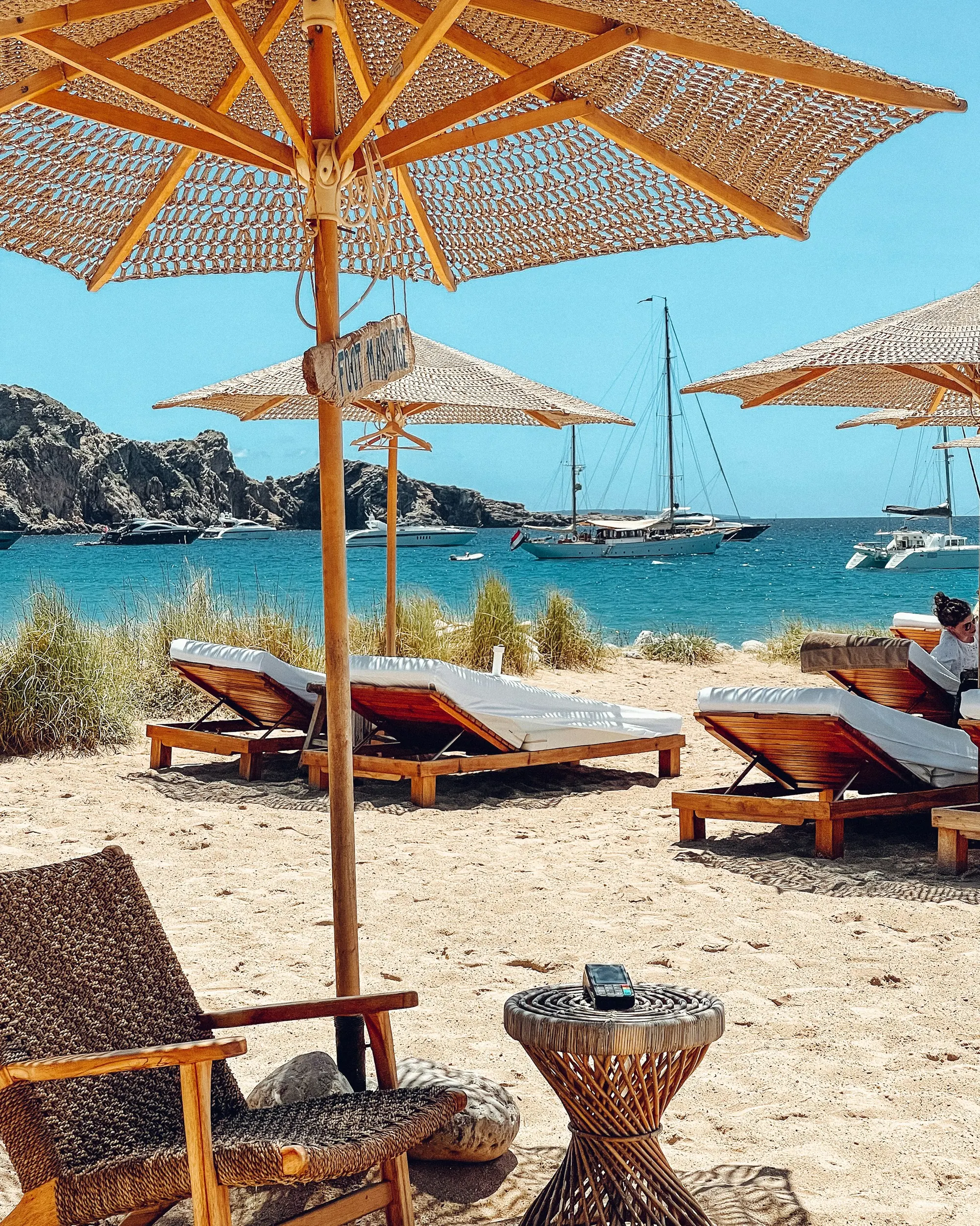 Sun loungers and parasols on a beach club terrace above a turquoise bay