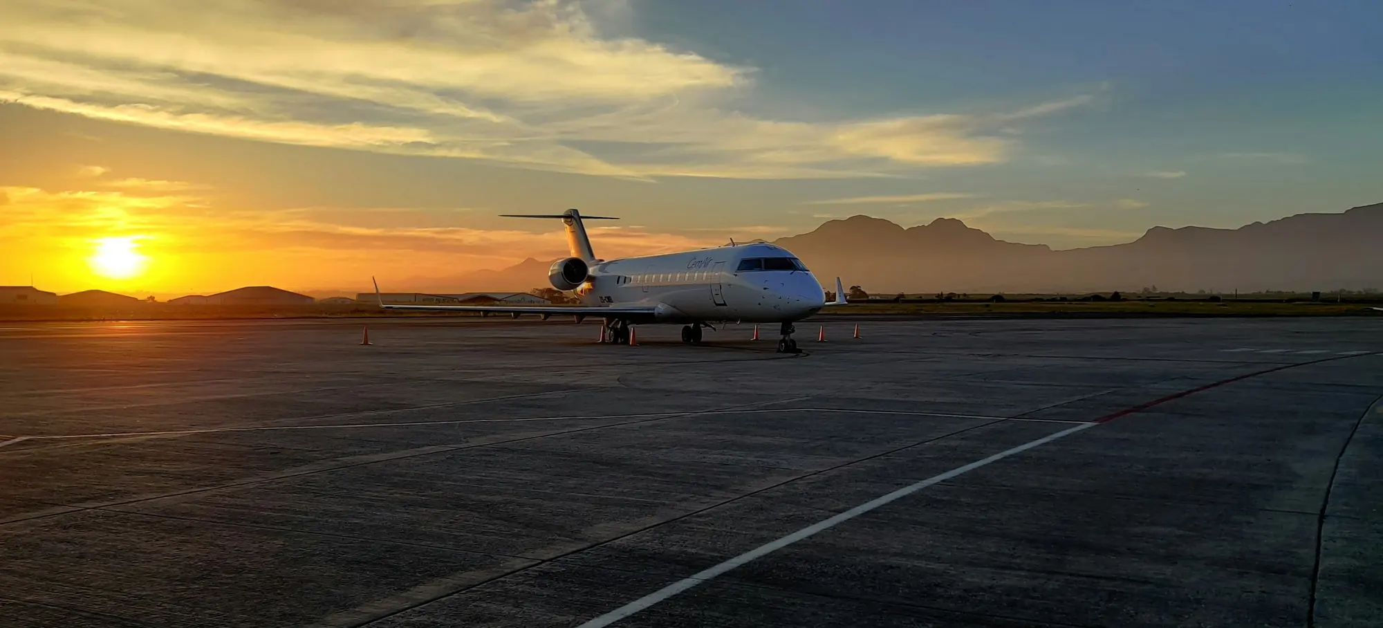 A business jet parked on the ramp at sunset with mountains behind