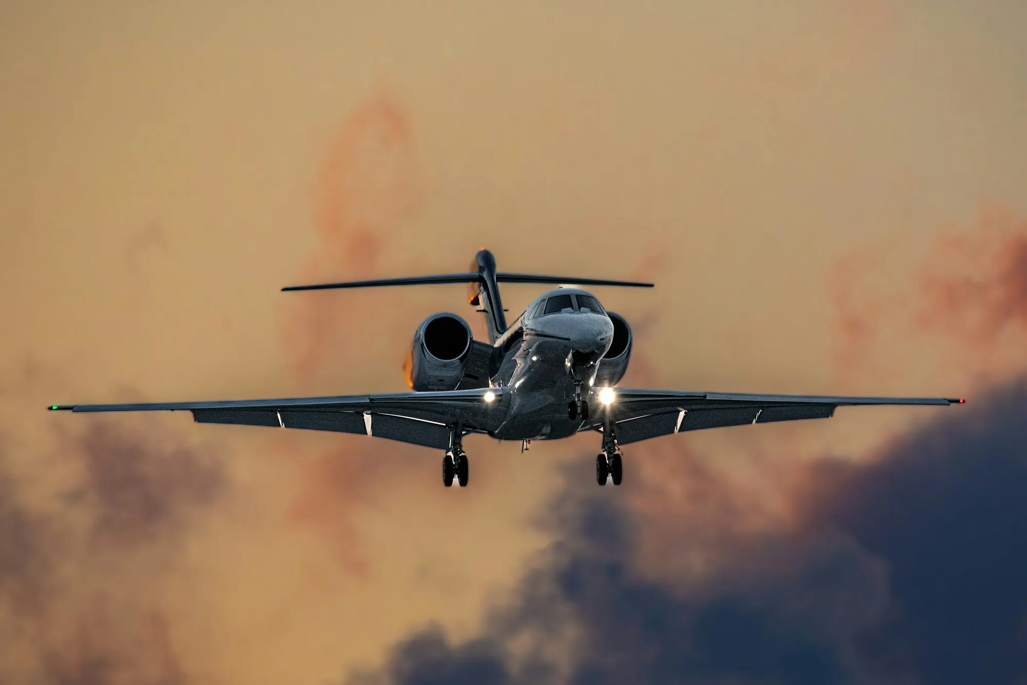 A long-range business jet descending through orange evening cloud